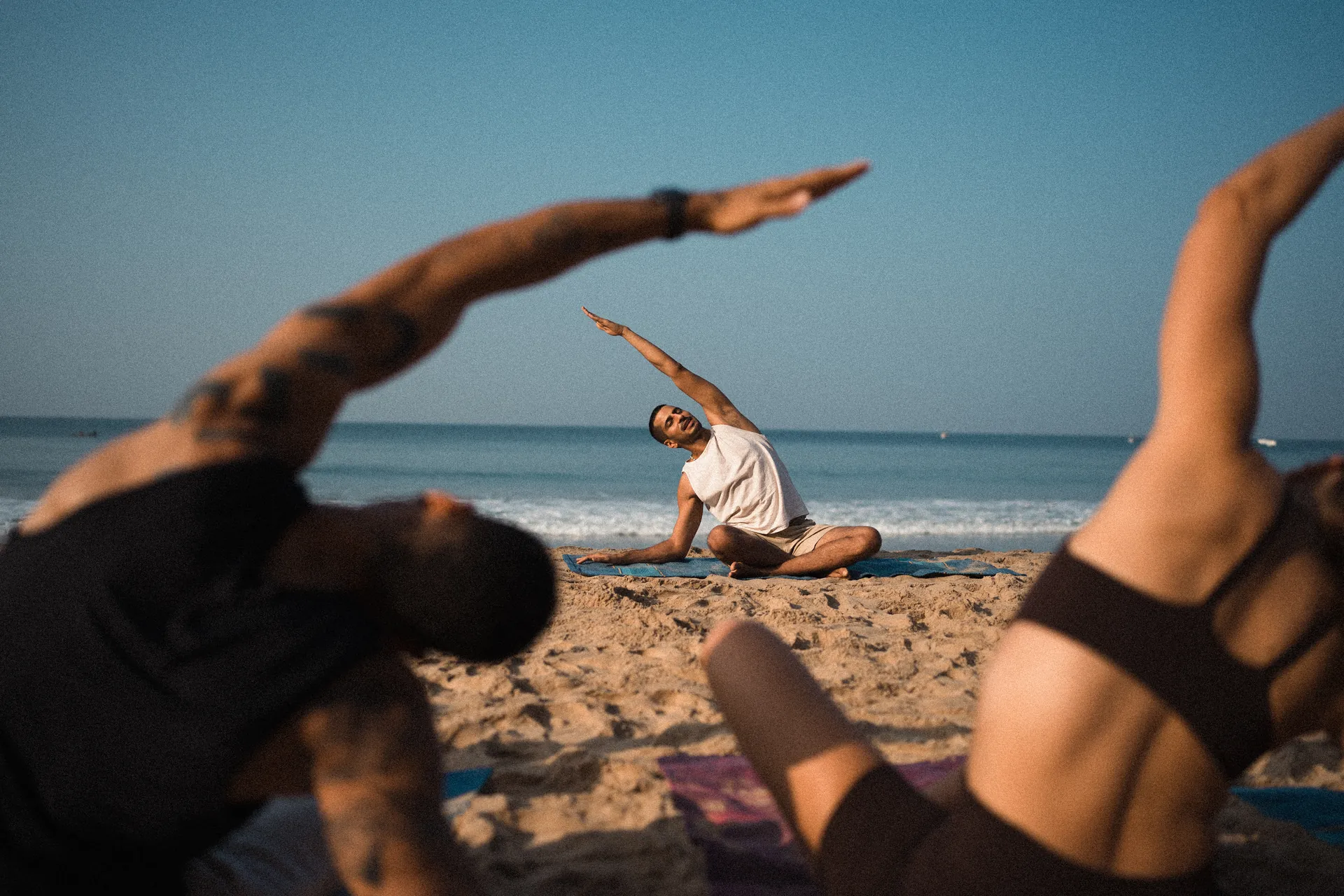 Students in a seated side stretch on beach mats facing the sea