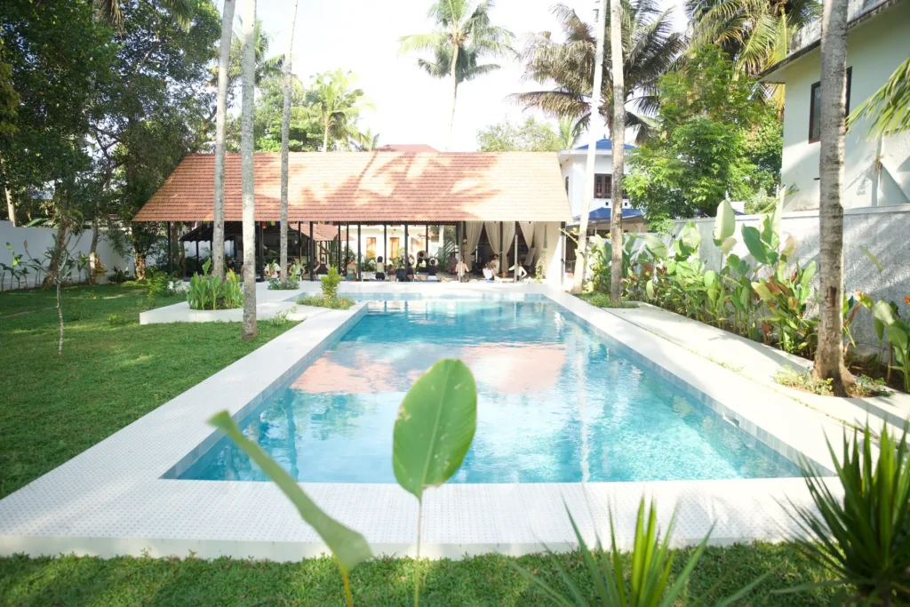 Swimming pool lined with palm trees leading to the open shala where a class is under way
