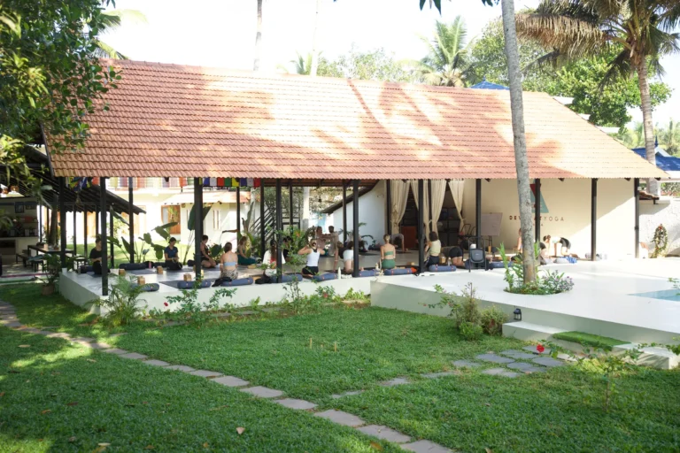 Open sided shala with students practising on mats, seen across the lawn