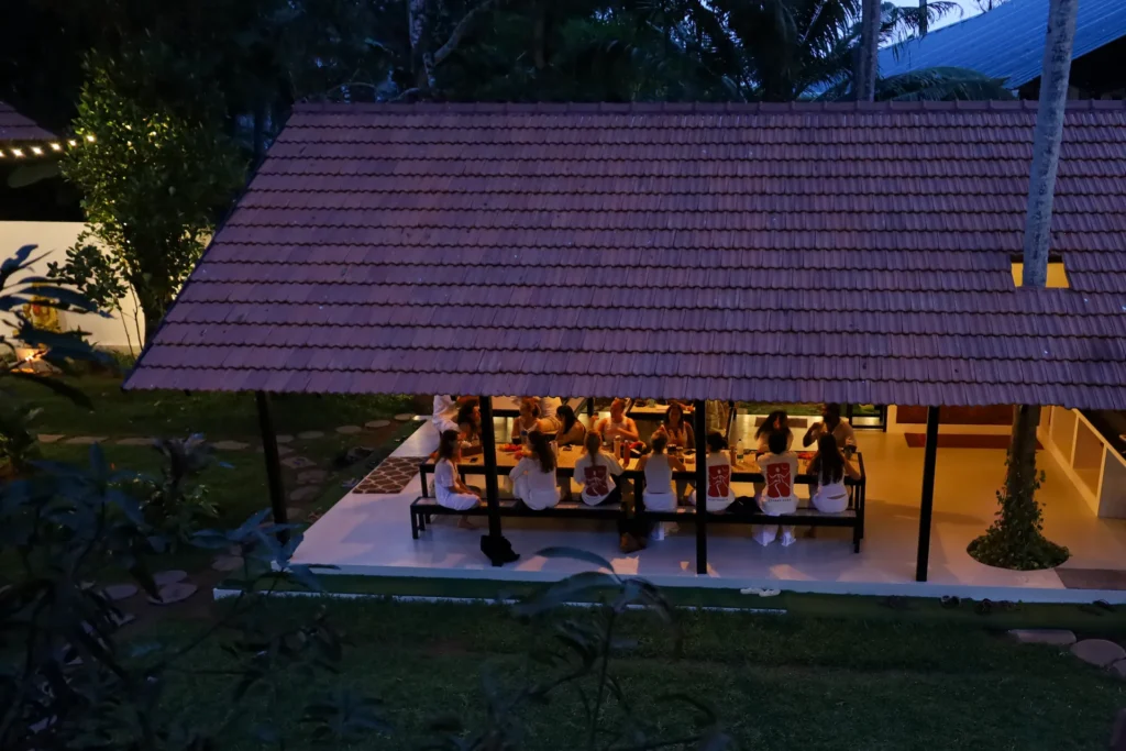 Students eating at long tables in the lit dining pavilion at night, seen from above
