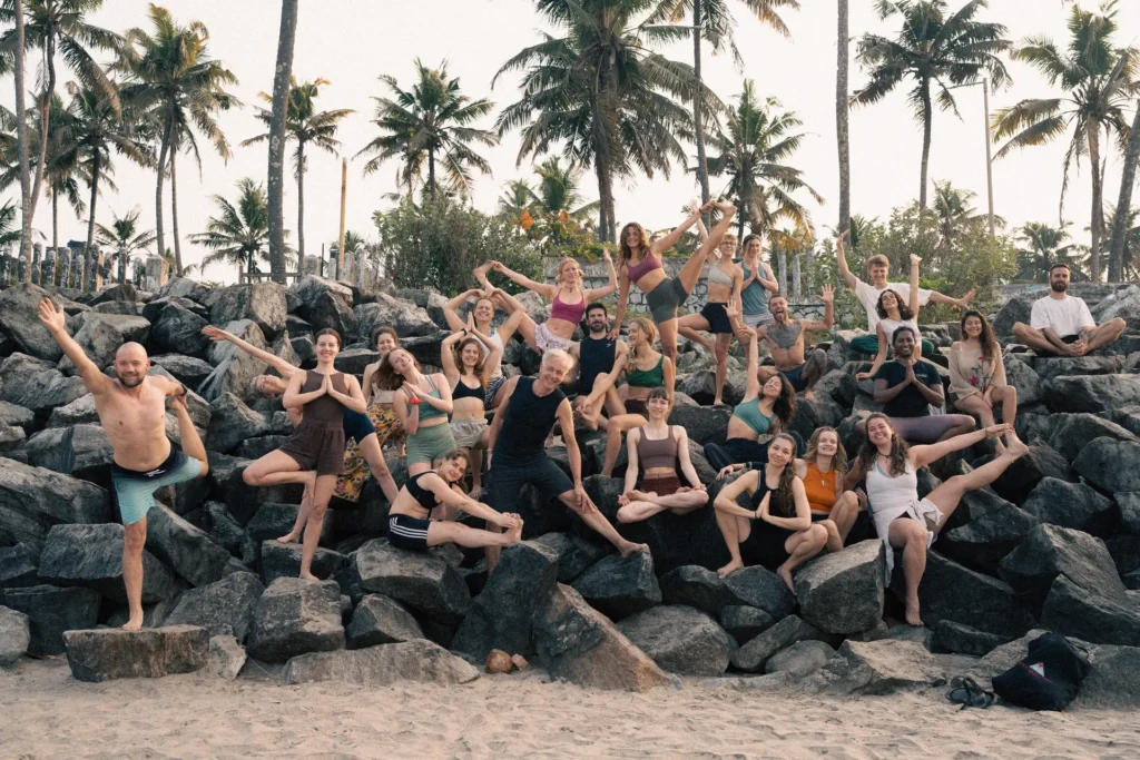 Large group holding yoga poses on the rocks at Varkala beach under palm trees