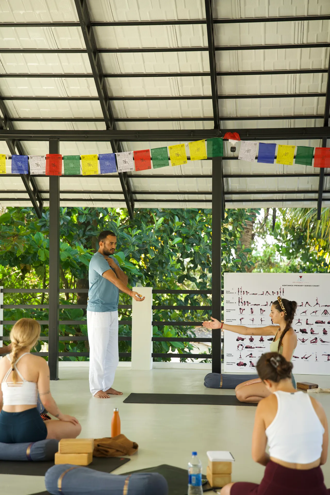 Man in a blue shirt demonstrating to seated students under rows of prayer flags